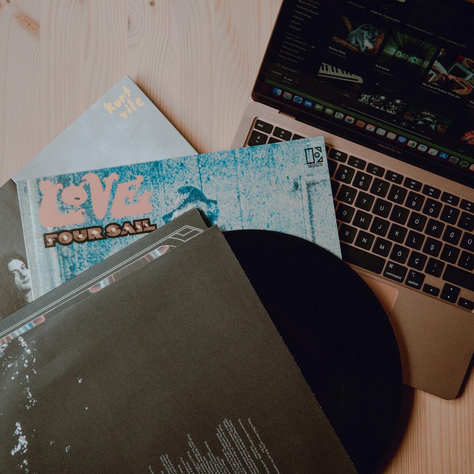 Une table de rédaction vue de dessus : un carnet, un ordinateur, des pochettes de disques